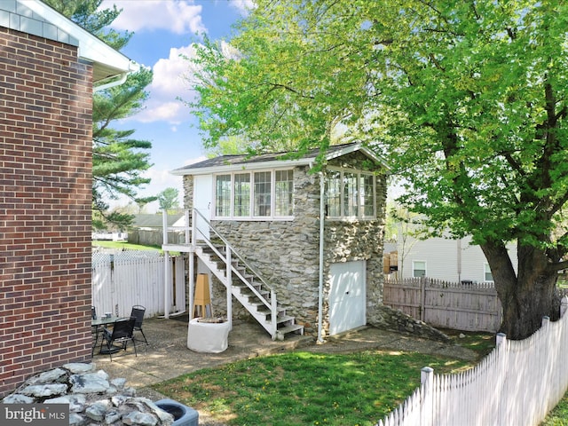 rear view of house with stone siding, a fenced backyard, and stairs