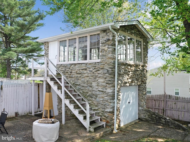 view of side of home featuring stone siding, stairs, and fence