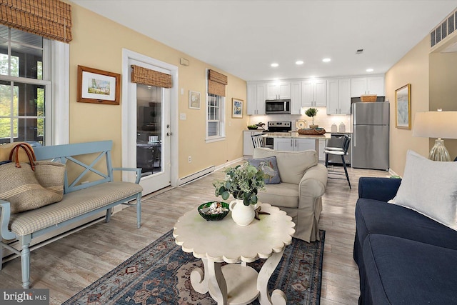 living room featuring visible vents, light wood-type flooring, baseboards, a baseboard heating unit, and recessed lighting