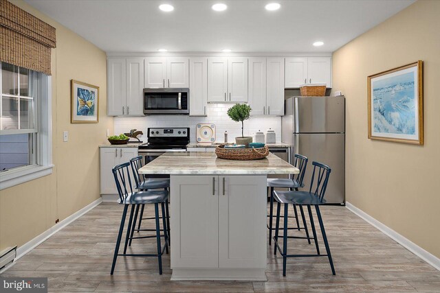 kitchen with light wood-style floors, a breakfast bar area, backsplash, and stainless steel appliances