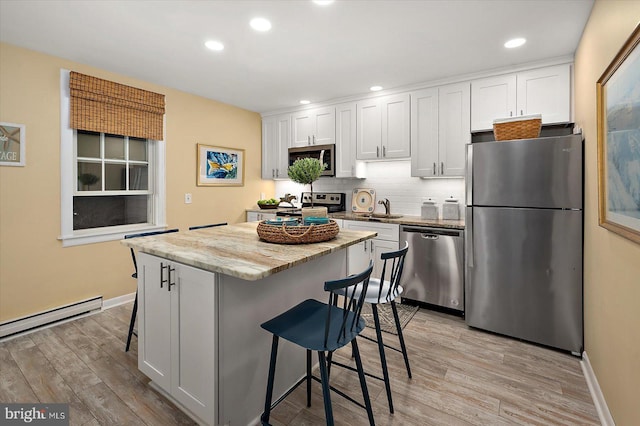 kitchen featuring a kitchen breakfast bar, a center island, a sink, light wood-style floors, and stainless steel appliances