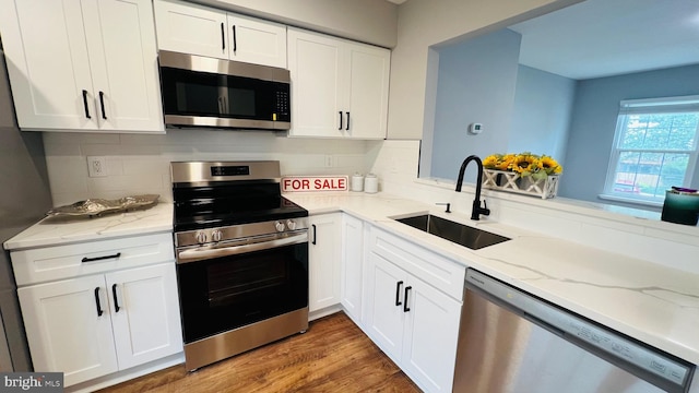 kitchen with appliances with stainless steel finishes, a sink, white cabinetry, decorative backsplash, and light stone countertops