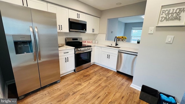 kitchen with appliances with stainless steel finishes, a sink, white cabinets, and light wood finished floors