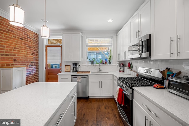 kitchen featuring white cabinets, a sink, brick wall, decorative light fixtures, and appliances with stainless steel finishes