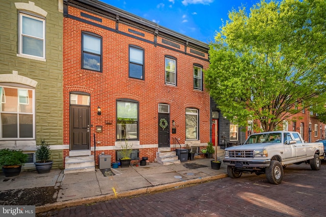 townhome / multi-family property featuring entry steps, uncovered parking, and brick siding