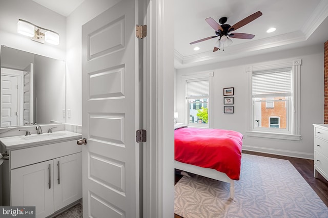 bedroom featuring a sink, a raised ceiling, baseboards, ornamental molding, and dark wood-style floors