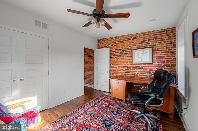 office with wood finished floors, visible vents, a ceiling fan, baseboards, and brick wall