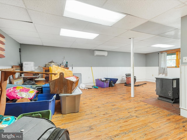 below grade area featuring a wall mounted AC, wainscoting, wood finished floors, and a paneled ceiling