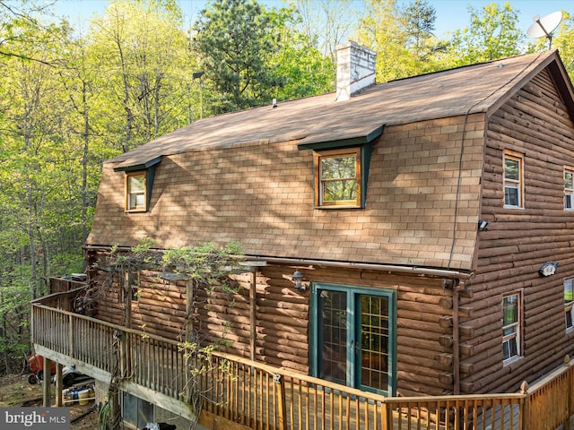 view of home's exterior with a shingled roof, a wooden deck, a gambrel roof, and log exterior
