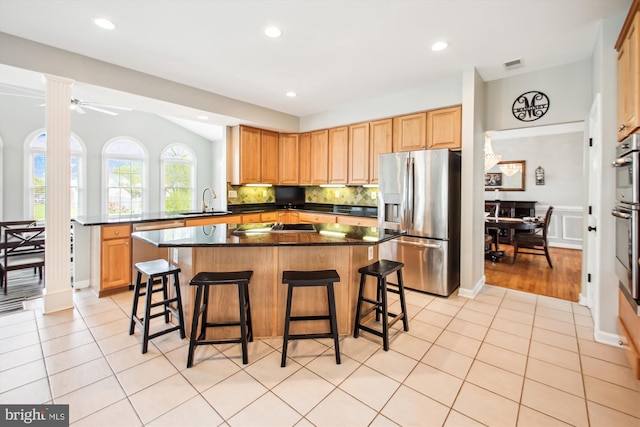 kitchen with a sink, dark countertops, visible vents, a kitchen bar, and stainless steel refrigerator with ice dispenser