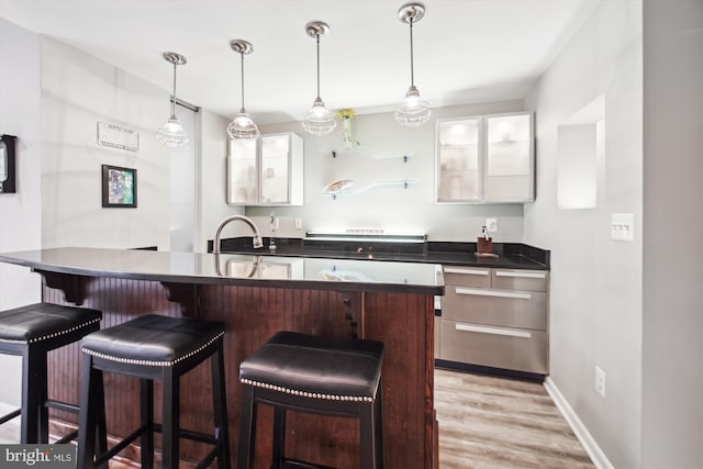 kitchen with white cabinetry, light wood-style floors, a kitchen bar, and a sink