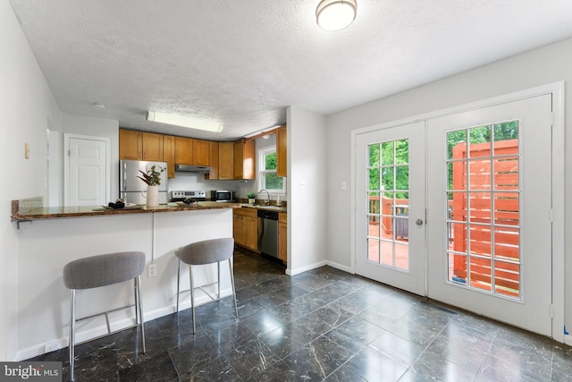 2116 Bell Tree Ln, Waldorf, MD 20601 - kitchen with appliances with stainless steel finishes, under cabinet range hood, a sink, a textured ceiling, and brown cabinetry