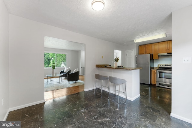 2116 Bell Tree Ln, Waldorf, MD 20601 - kitchen featuring appliances with stainless steel finishes, under cabinet range hood, brown cabinets, baseboards, and a textured ceiling