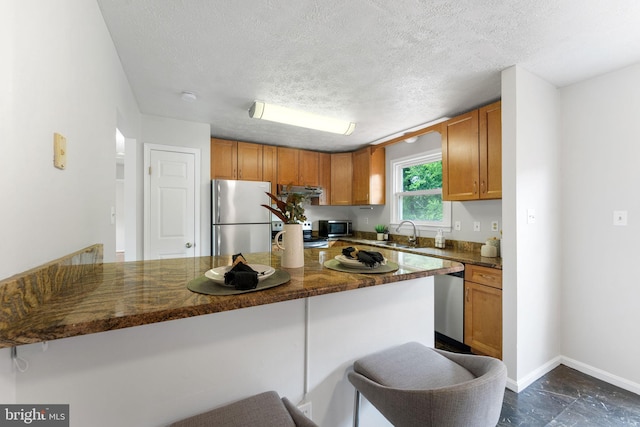 2116 Bell Tree Ln, Waldorf, MD 20601 - kitchen featuring appliances with stainless steel finishes, a sink, a peninsula, brown cabinetry, and a breakfast bar