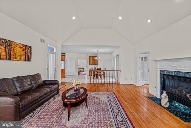 living room featuring recessed lighting, a premium fireplace, light wood-type flooring, a chandelier, and high vaulted ceiling