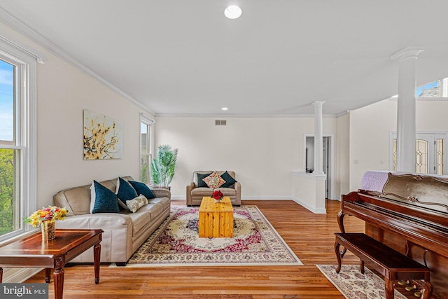 living area with wood finished floors, plenty of natural light, decorative columns, and visible vents