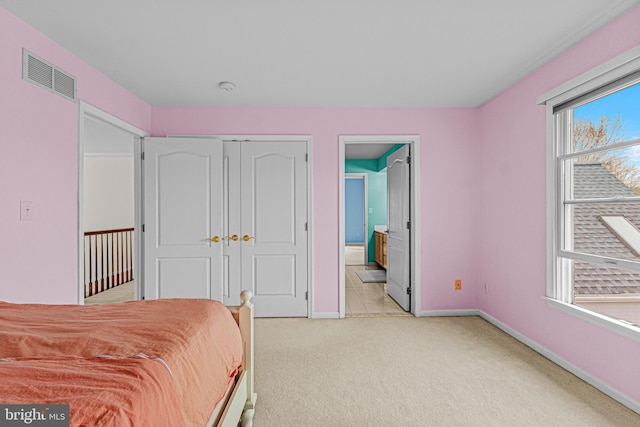 bedroom featuring a closet, connected bathroom, light carpet, baseboards, and visible vents