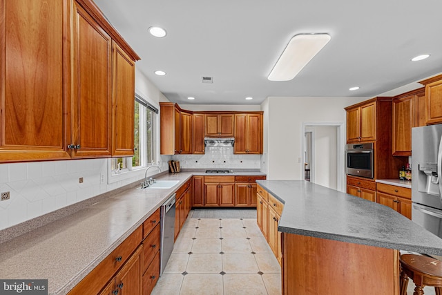 kitchen featuring a center island, tasteful backsplash, a sink, brown cabinets, and appliances with stainless steel finishes