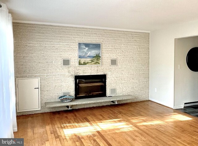unfurnished living room with a brick fireplace, baseboards, visible vents, and wood finished floors