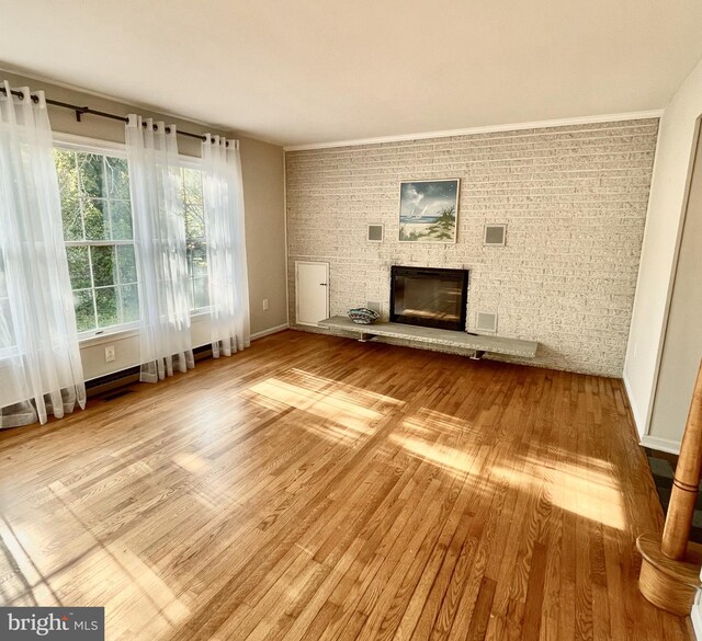 unfurnished living room with visible vents, wood finished floors, brick wall, and a fireplace