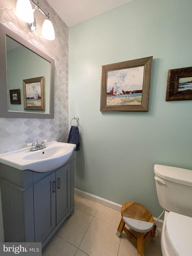 half bath featuring vanity, baseboards, tile patterned floors, and toilet