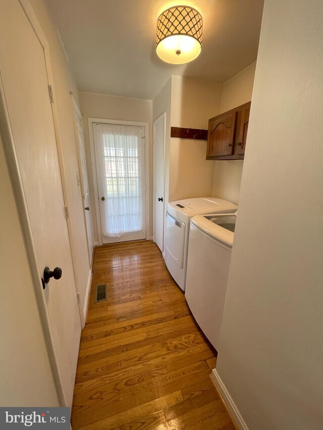 clothes washing area with visible vents, baseboards, cabinet space, washing machine and clothes dryer, and light wood finished floors