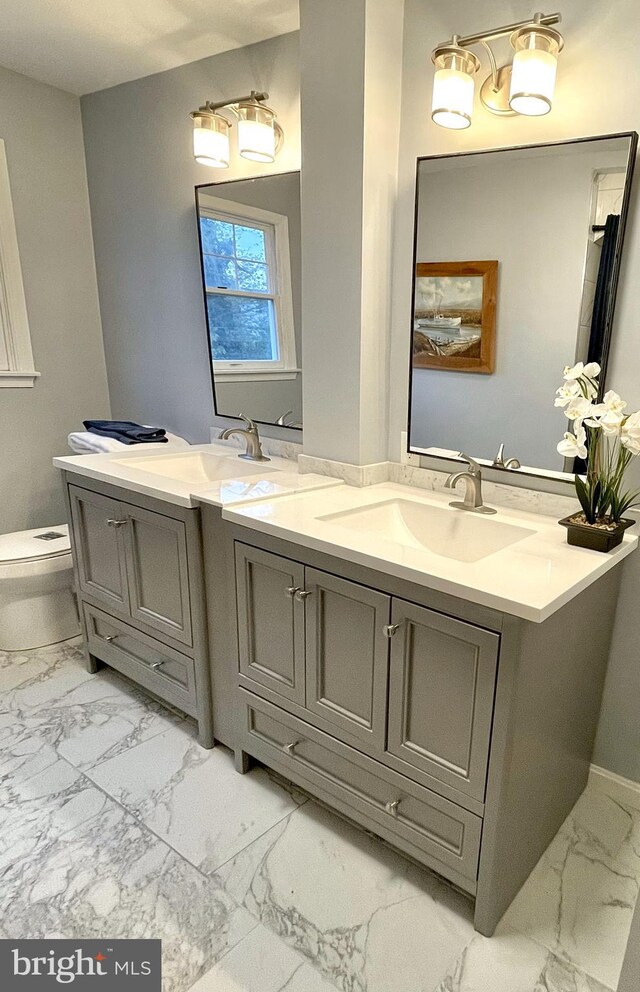bathroom featuring double vanity, toilet, a sink, and marble finish floor