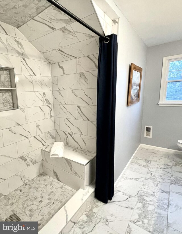 bathroom featuring baseboards, marble finish floor, a tile shower, and toilet