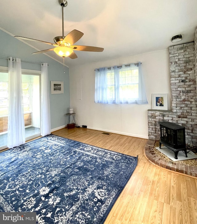 living room with ceiling fan, plenty of natural light, wood finished floors, and a wood stove