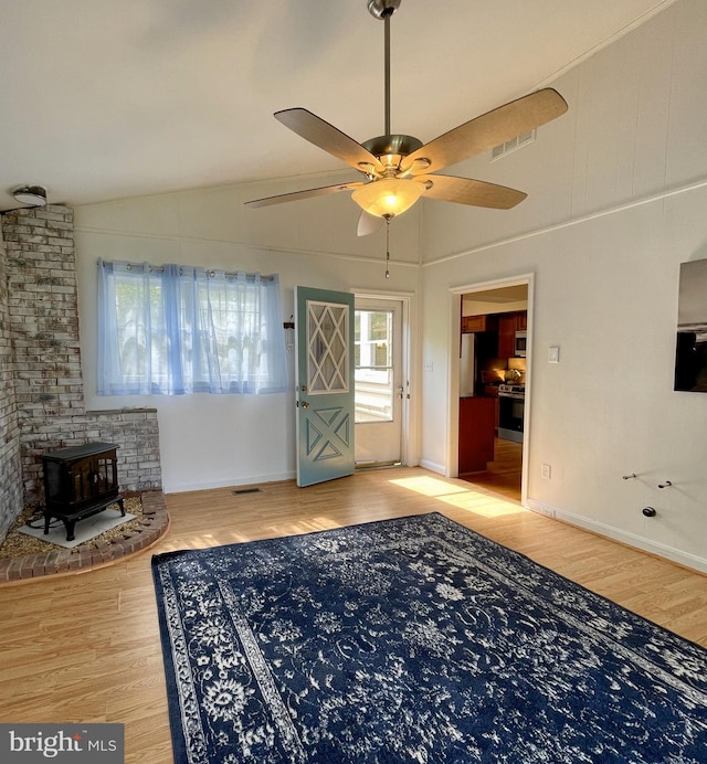 living area with ceiling fan, visible vents, vaulted ceiling, a wood stove, and wood finished floors