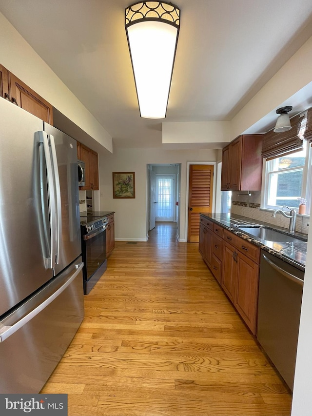 kitchen featuring a sink, stainless steel appliances, brown cabinetry, light wood-type flooring, and baseboards
