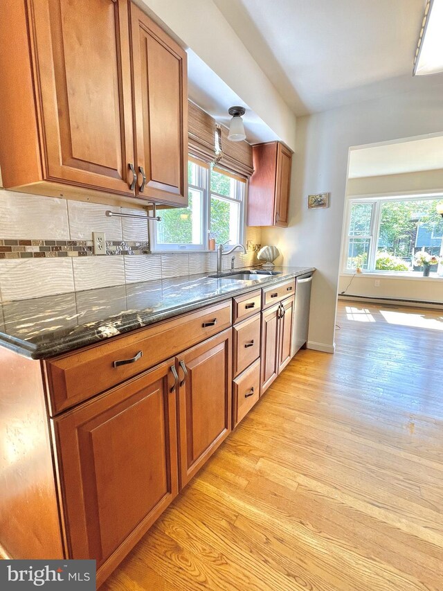 kitchen featuring a sink, decorative backsplash, dark stone countertops, and light wood-style flooring