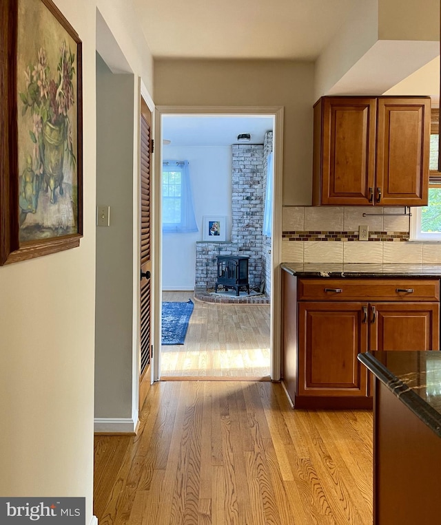 kitchen with decorative backsplash, brown cabinetry, a wood stove, and light wood-style floors
