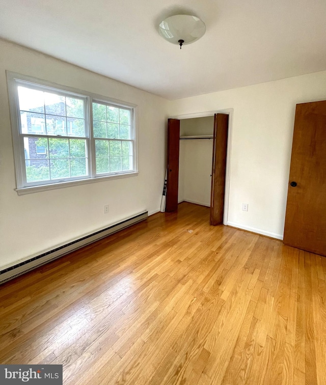 unfurnished bedroom with a closet, light wood finished floors, and baseboard heating