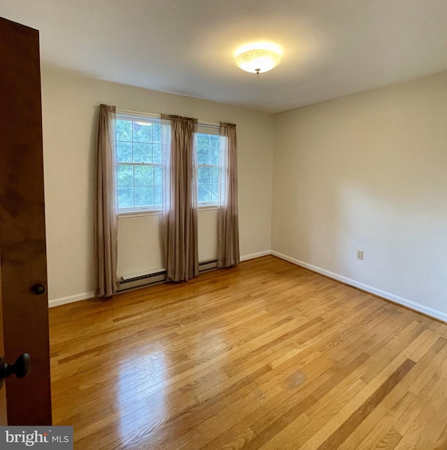 empty room with light wood-type flooring, baseboards, and a baseboard heating unit
