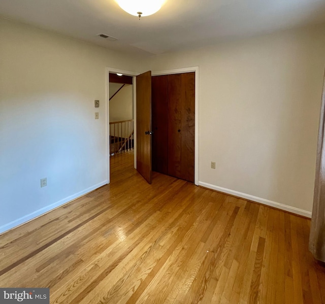 unfurnished bedroom with a closet, baseboards, visible vents, and light wood-style floors