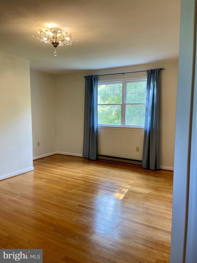 spare room with baseboards, a baseboard radiator, wood finished floors, and a chandelier