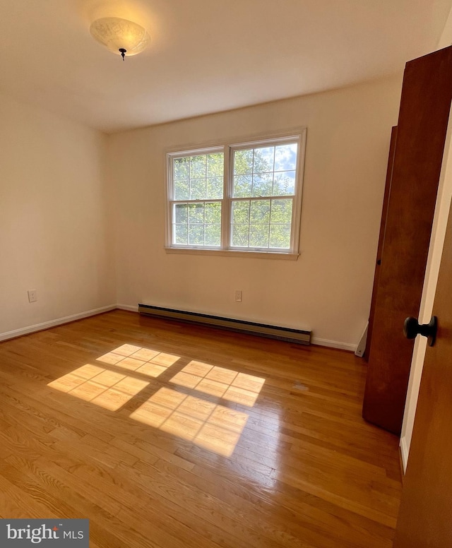 spare room featuring wood finished floors, baseboards, and a baseboard heating unit