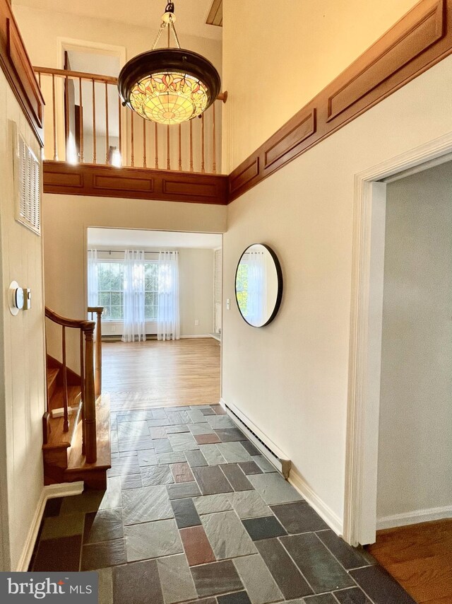 interior space with baseboards, stone finish flooring, a towering ceiling, and baseboard heating