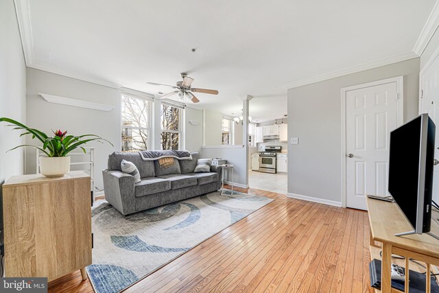 living room featuring a ceiling fan, light wood-style floors, baseboards, ornamental molding, and ornate columns