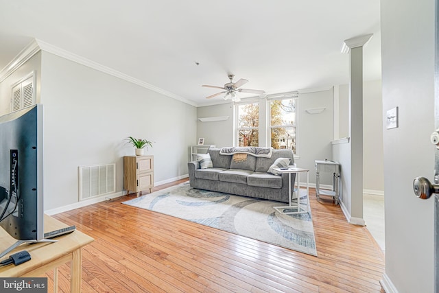 living room with light wood finished floors, baseboards, visible vents, a ceiling fan, and crown molding