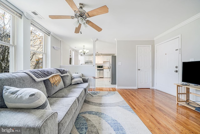 living area with crown molding, ceiling fan with notable chandelier, light wood-style flooring, baseboards, and visible vents