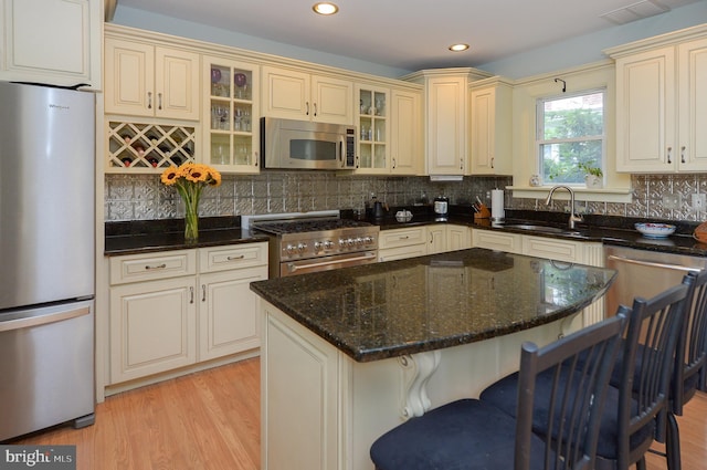 kitchen featuring stainless steel appliances, a sink, cream cabinets, dark stone countertops, and recessed lighting