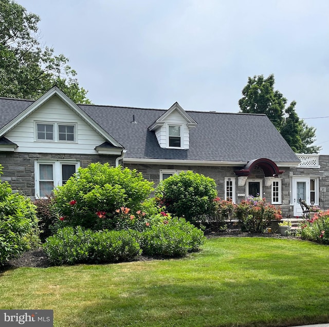 cape cod house with stone siding, a front lawn, and a shingled roof