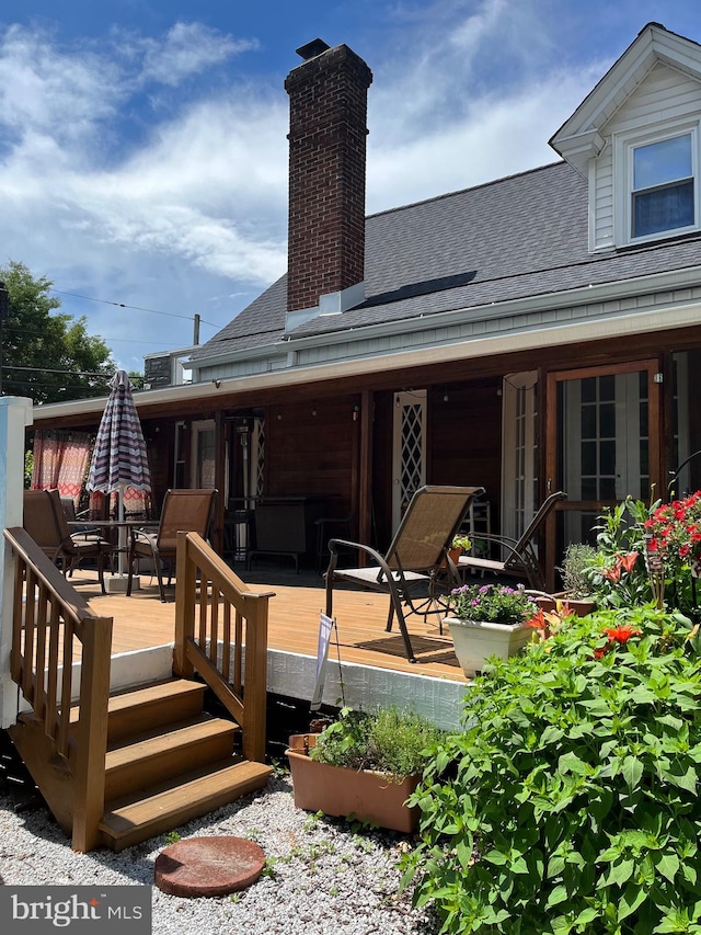 rear view of house with roof with shingles, a chimney, a wooden deck, and outdoor dining area