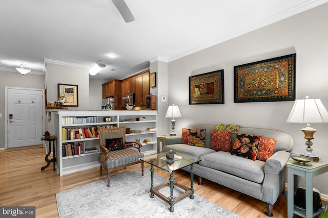 living area featuring light wood-type flooring, ornamental molding, baseboards, and a ceiling fan