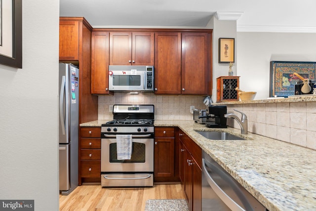 kitchen featuring crown molding, decorative backsplash, light wood-type flooring, a sink, and stainless steel appliances