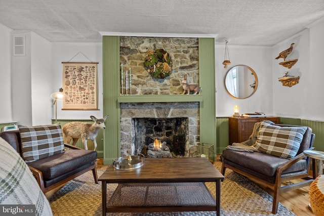 sitting room with a textured ceiling, wood finished floors, wainscoting, a fireplace, and visible vents