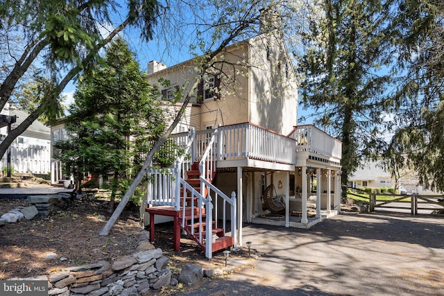 back of house with stairway, a chimney, fence, stucco siding, and a wooden deck