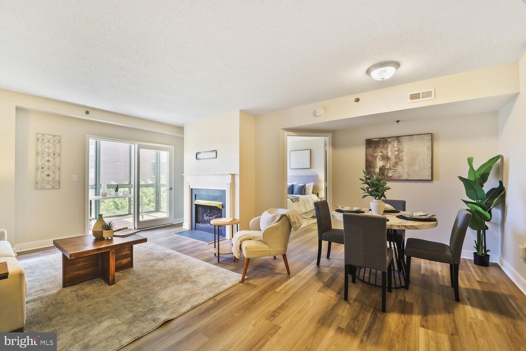 dining area featuring a fireplace with flush hearth, a textured ceiling, baseboards, visible vents, and wood finished floors